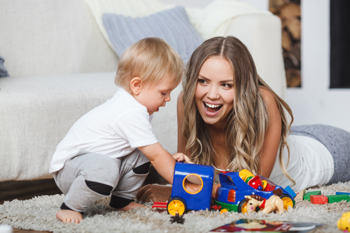 cute blonde mother and child boy play together indoors at home on the carpet